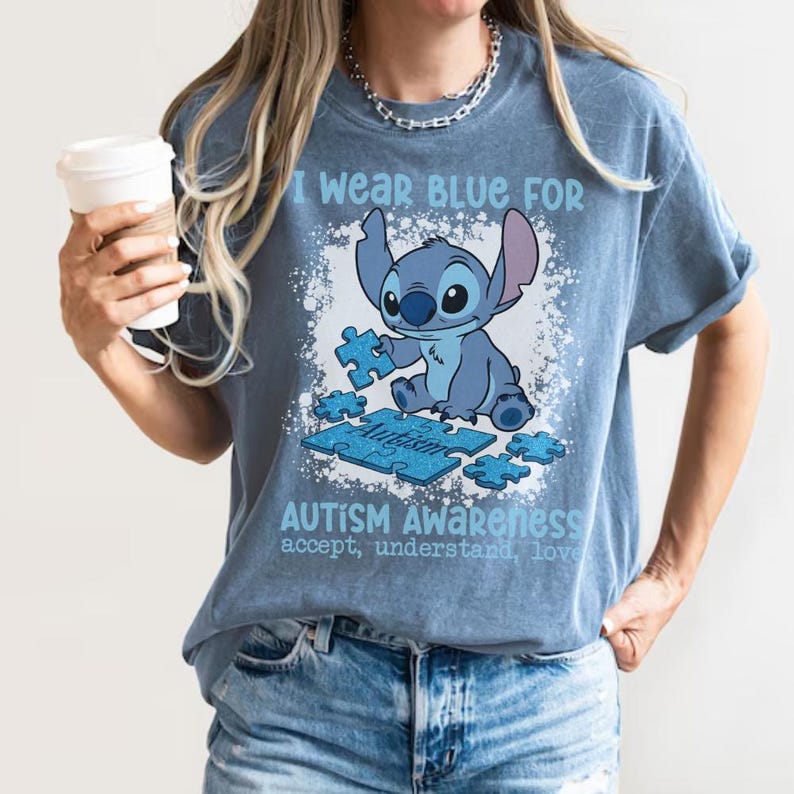 K&ouml;nnte beinhalten: Blaues T-Shirt mit dem Text "I wear blue for Autism Awareness" und einer Cartoonfigur, die ein Puzzleteil h&auml;lt. Das Shirt hat auch die Worte "accept, understand, love".
