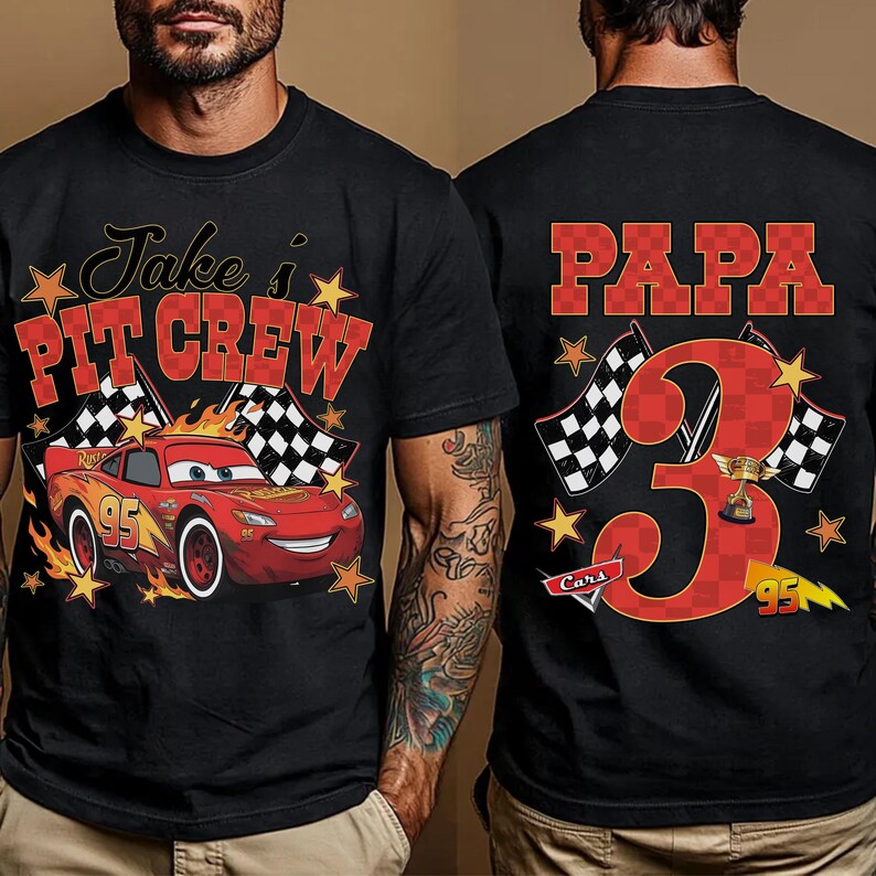 Puede incluir: Una camiseta negra con un gr&aacute;fico de un coche de carreras rojo con el n&uacute;mero 95, banderas a cuadros, estrellas amarillas y el texto Jake's PIT CREW en el frente. La parte trasera muestra el texto PAPA, un n&uacute;mero 3 grande y un trofeo.