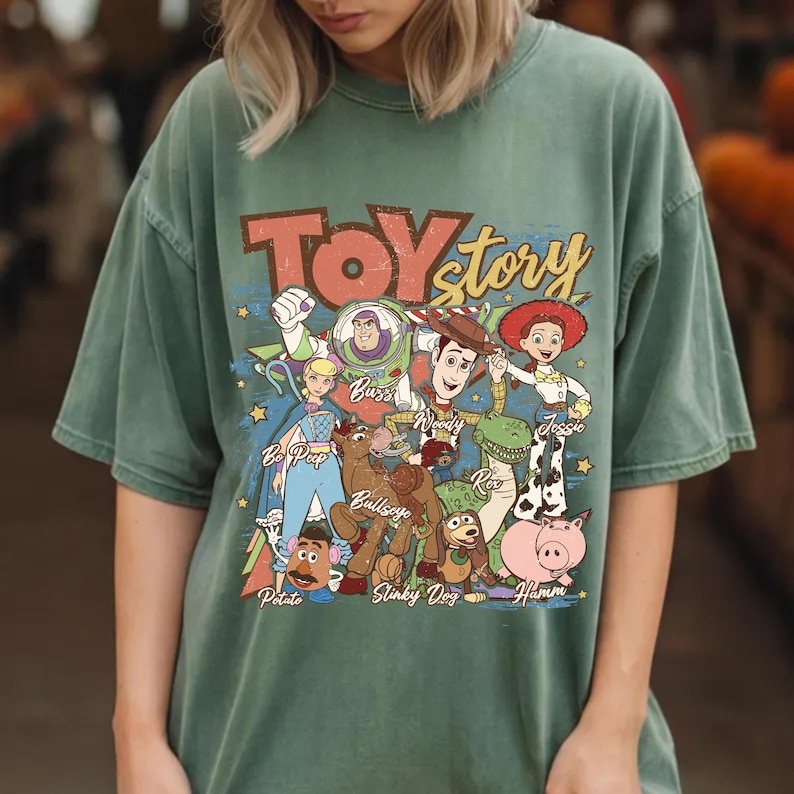 Puede incluir: Camiseta verde con la frase "Toy Story" en una fuente retro y un gr&aacute;fico de personajes de la pel&iacute;cula animada. Los personajes incluyen a Buzz Lightyear, Woody, Jessie y otros. La camiseta tiene un aspecto vintage.