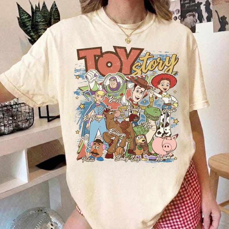 Puede incluir: Camiseta de color crema con un gr&aacute;fico colorido de personajes de la pel&iacute;cula animada "Toy Story". El dise&ntilde;o incluye a Woody, Buzz Lightyear, Jessie y otros personajes, con las palabras "Toy Story" en una fuente desgastada.
