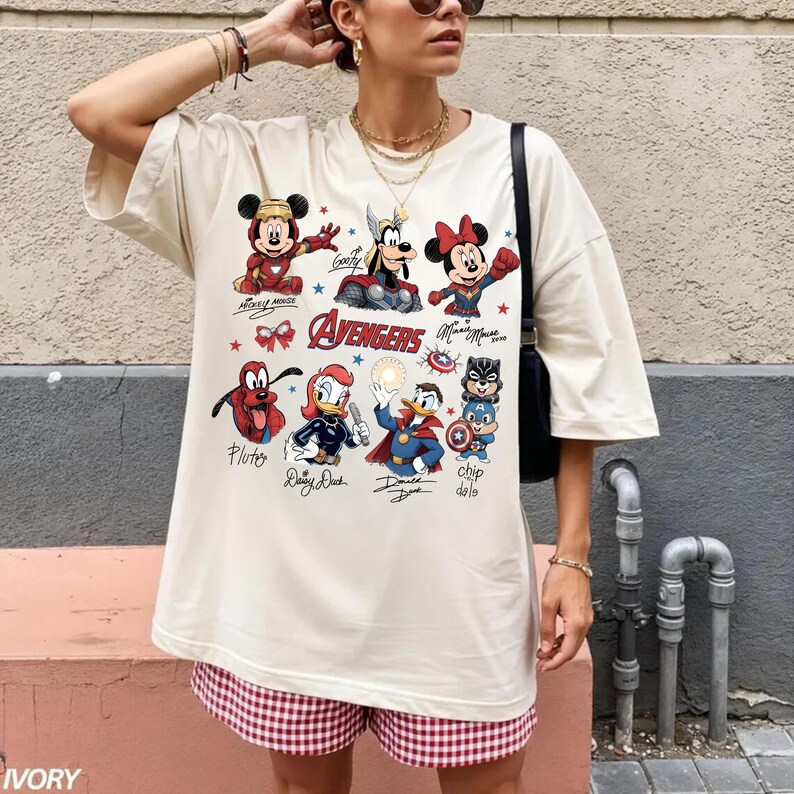 May include: An ivory-coloured oversized t-shirt with a colourful graphic of Disney characters as Avengers. The design includes Mickey Mouse, Minnie Mouse, Goofy, Pluto, Daisy Duck, Donald Duck, and Chip and Dale. The word "Avengers" is also printed on the shirt.