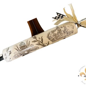May include: A white rolling pin with a black and white checkered handle. The rolling pin is decorated with a black and white floral design and a crown. The rolling pin is tied with a white ribbon and a black and white checkered ribbon.