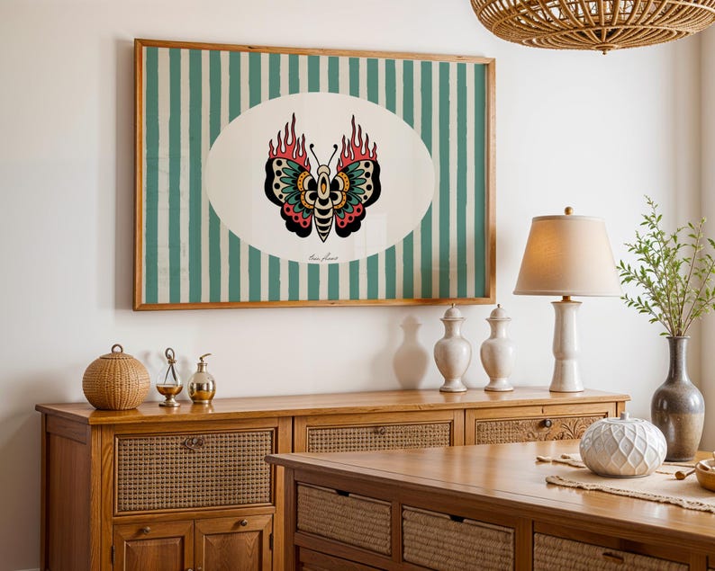 May include: A framed artwork featuring a butterfly design with flames, set against a background of vertical teal and white stripes. The butterfly has black, red, and teal details. The artwork is displayed above a wooden cabinet.
