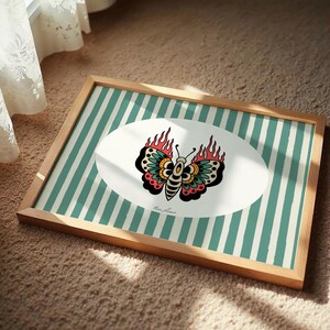 May include: Framed art print with a butterfly design, flames, and teal stripes. The artwork is in a wooden frame. The butterfly is in an oval shape. The artwork is in a wooden frame.