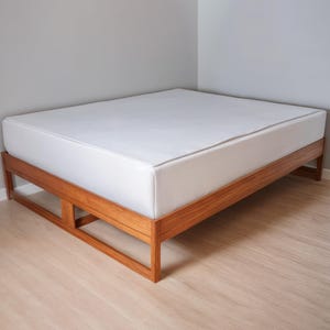 May include: A wooden bed frame with a white mattress. The frame has a slatted design and is made of natural wood.