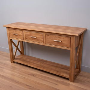 May include: A wooden console table with three drawers and a lower shelf. The table has a natural wood finish and a simple, modern design.