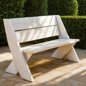 Puede incluir: Banco de madera blanco con un diseño sencillo, con un asiento ancho y patas inclinadas. El banco está hecho de madera natural y tiene una sensación ligera y aireada.