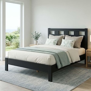 May include: A black wooden bed frame with a headboard featuring a grid design. The bed is made up with white bedding, decorative pillows, and a light green throw blanket. A light blue rug is on the floor.