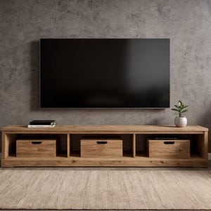 May include: A light-coloured wooden TV stand with three drawers and open shelving. A large black television is mounted on the grey wall above the stand. A small potted plant and books are on the stand.