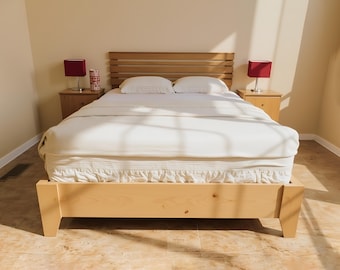 May include: A light-colored wooden bed frame with a matching headboard. The bed is made up with white bedding, including a fitted sheet, a ruffled bed skirt, and a blanket. Two matching nightstands with red lamps are on either side of the bed.