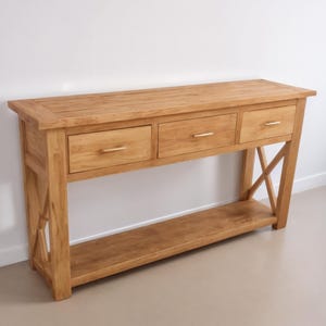 May include: A light wood console table with three drawers and a lower shelf. The table has a simple, traditional design with X-shaped legs.