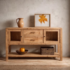 May include: A light brown wooden sideboard with two drawers and two glass-door cabinets. A framed picture of a maple leaf, a brown pitcher, a wooden bowl with an orange fruit, and a woven basket are on the sideboard.