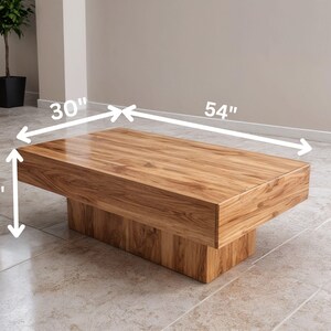 May include: A rectangular wooden coffee table with a natural wood grain finish. The table is 137 cm long, 76 cm wide, and 36 cm high. The table has a solid base and a simple, modern design.