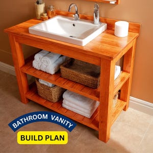 以下が含まれることがあります： 白い洗面台とクロム製の蛇口が付いた木製の洗面化粧台。白いタオルと籐のバスケットが入った2つの棚があります。洗面化粧台は温かみのあるオレンジ色に着色されています。「BATHROOM VANITY BUILD PLAN」というテキストが表示されています。