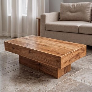 May include: A rectangular wooden coffee table with a natural wood grain finish. The table has a solid, blocky design with a lower base and a wide top. The table is approximately 122 cm long and 61 cm wide.