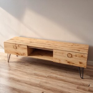 Puede incluir: Un mueble de TV de madera clara con dos cajones y un estante central abierto. El mueble tiene un acabado de vetas de madera natural, tiradores redondos y patas de horquilla de metal negro. Mide aproximadamente 152 cm de largo.