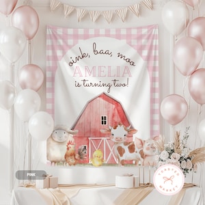 May include: A pink and white party backdrop with balloons and a banner. The backdrop features a barn scene with farm animals and the text "oink, baa, moo" and "AMELIA is turning two!" A table holds gifts and a cake.