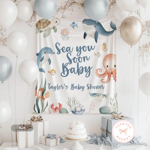 May include: A baby shower backdrop with an ocean theme, featuring illustrations of sea creatures like a whale, dolphin, and octopus. The text "Sea you Soon Baby" and "Taylor's Baby Shower" are displayed. White and blue balloons and gifts surround the backdrop.