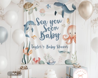 May include: A baby shower backdrop with an ocean theme, featuring illustrations of sea creatures like a whale, dolphin, and octopus. The text "Sea you Soon Baby" and "Taylor's Baby Shower" are displayed. White and blue balloons and gifts surround the backdrop.