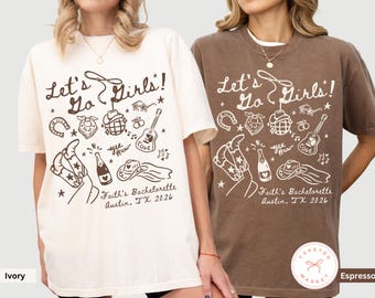 May include: Two t-shirts, one ivory and one espresso, feature a graphic design with the text "Let's Go Girls!" and various illustrations including a horseshoe, cowboy hat, and guitar. The text "Faith's Bachelorette Austin, TX 2026" is also present.