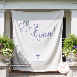 May include: White tapestry with violet text that reads "He is Risen!" and a cross, with "Matthew 28:6" below. The tapestry is hanging on a porch, flanked by potted plants.