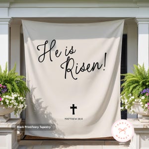 May include: Ivory tapestry with black script reading "He is Risen!" and a cross, with "MATTHEW 28:6" below. The tapestry is hanging on a porch, flanked by potted plants. The words "Black Print/Ivory Tapestry" are at the bottom.