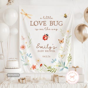May include: A white baby shower backdrop with the text "a little LOVE BUG is on the way" and "Emily's BABY SHOWER 04.11.26". The backdrop features watercolor illustrations of a dragonfly, bee, ladybug, butterflies, and flowers. White and gold balloons are visible.