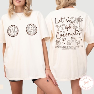 May include: Ivory-colored t-shirt with two brown coconut illustrations on the front. The back of the shirt features the text "Let's go Coconuts" with tropical-themed graphics, including a palm tree and cocktails. "Madison's Bachelorette Charleston, SC" is also printed on the back.
