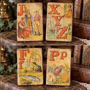 May include: Four rectangular wooden blocks featuring vintage-style illustrations and letters. One block shows Jj with figures, another XYZ with a ship and zebra, one Ff with a frog and fish, and one Pp with a parrot, flower, and pineapple.
