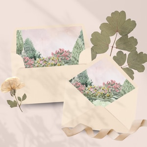 Peut inclure: Deux enveloppes crème avec des illustrations de paysages à l'aquarelle. L'art représente une scène de jardin avec des fleurs roses et des arbres verts. Une fleur séchée et des feuilles vertes sont disposées près des enveloppes.