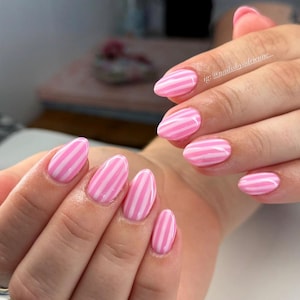 May include: Close-up of manicured nails with a pink and white striped design. The oval-shaped nails are painted with a glossy finish. The image includes the Instagram handle @nailssbyadrienne.
