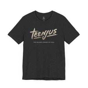 Puede incluir: Camiseta gris oscuro con el texto "TEENJUS" en una fuente estilizada de color blanquecino, con la frase "THE SECOND COMING OF COOL" debajo. La camiseta tiene cuello redondo y mangas cortas.