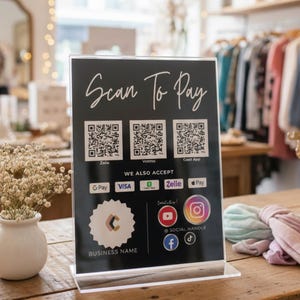 May include: A black sign with the words "Scan To Pay" in white script. The sign displays QR codes for Zelle, Venmo, and Cash App, along with payment options like GPay, Visa, and Zelle. The sign also includes social media icons.