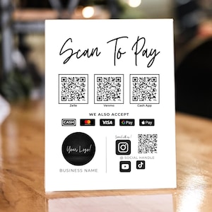 May include: White sign with black text that reads "Scan To Pay". The sign has three QR codes, one for each of the following payment methods: Zelle, Venmo, and Cash App. The sign also includes a section that reads "We Also Accept" and shows icons for cash, Visa, Google Pay, and Apple Pay. The sign also includes a space for a logo and social media handles.