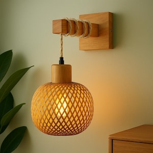 May include: A wooden wall sconce with a woven, spherical lampshade. The fixture features a square wooden base, a rectangular wooden arm wrapped with rope, and a round, woven lampshade. The light is warm and inviting, perfect for adding a touch of natural style.