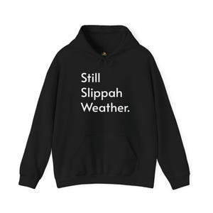 Pode incluir: Moletom preto com a frase branca "Still Slippah Weather". O moletom tem um bolso frontal e um capuz com cordão. Uma peça de roupa casual e confortável.
