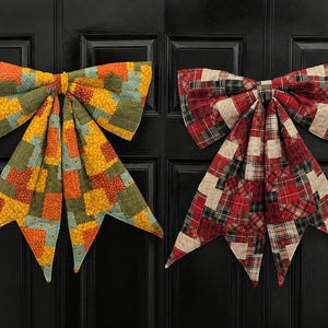 May include: Two decorative fabric bows featuring quilted patchwork designs. The left bow displays yellow, orange, and green squares with small patterns. The right bow features a red, black, and cream plaid patchwork pattern with quilted stitching.