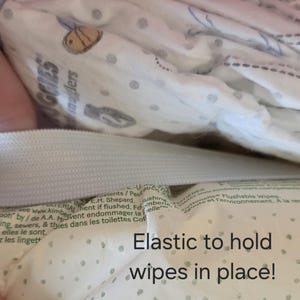 May include: Close-up of a Huggies Snugglers wipes package. The white packaging features a pattern of small grey dots and cartoon illustrations. The text "Elastic to hold wipes in place!" is visible.