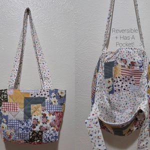 May include: A reversible patchwork tote bag with a floral print lining and a pocket. The exterior features a variety of fabric patterns, including floral, plaid, and striped designs. The bag has long straps for carrying.