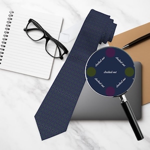 Può includere: Una cravatta blu navy con motivo geometrico, occhiali neri, un blocco note e una lente d'ingrandimento con la scritta "checked out" sono su una superficie di marmo. Sono visibili anche una penna e un laptop.