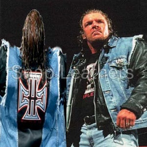 Puede incluir: Chaqueta vaquera con mangas de cuero negro y camiseta negra. La parte trasera de la chaqueta tiene un gran diseño de cruz blanca y roja. La chaqueta la lleva una persona con pelo largo.