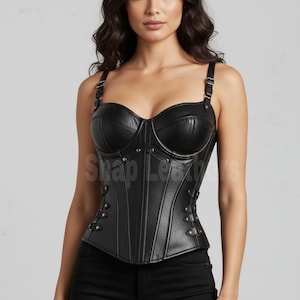 Puede incluir: Corsé de cuero negro con tirantes ajustables y busto estructurado. El corsé presenta paneles verticales y remaches decorativos. El texto "Shop Leathers" es visible en la prenda.