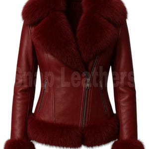 Pode incluir: Casaco de couro bordô com gola, punhos e acabamento em pele. O casaco tem fecho de correr e dois bolsos frontais com fecho. As mangas são compridas e o casaco tem uma silhueta ajustada. A pele é de cor vermelho escuro.