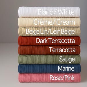 Peut inclure: Une pile de huit rouleaux de tissu de différentes couleurs : blanc, crème, beige, terre cuite foncée, terre cuite, sauge, marine et rose. Chaque rouleau est étiqueté avec son nom de couleur en texte blanc.