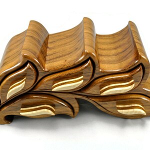 May include: A wooden jewelry box with a unique leaf design. The box has four compartments and is made of a light brown wood with a natural finish.