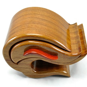 Könnte beinhalten: Eine Holzkiste mit einem einzigartigen wellenförmigen Design. Die Kiste ist aus hellbraunem Holz mit einem roten Akzent im Inneren.