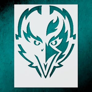 May include: White stencil featuring a stylized bird of prey design. The bird's head is the central focus, with sharp, angular details and a symmetrical arrangement. The design is cut out from a white rectangular sheet, creating a negative space effect.