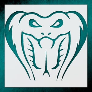 May include: A white stencil featuring a stylized cobra head with open mouth and fangs. The cobra's eyes are almond-shaped, and the design is set against a teal background. The cobra's hood is flared.
