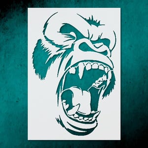 May include: A white stencil featuring a roaring gorilla head with sharp teeth and an open mouth. The gorilla's face is detailed with fur and facial features, creating a bold and aggressive design. The stencil is likely for art or crafts.