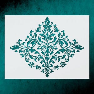 May include: A white stencil featuring a teal damask design. The damask pattern is symmetrical, with swirling leaves and floral elements. The stencil is on a teal background.